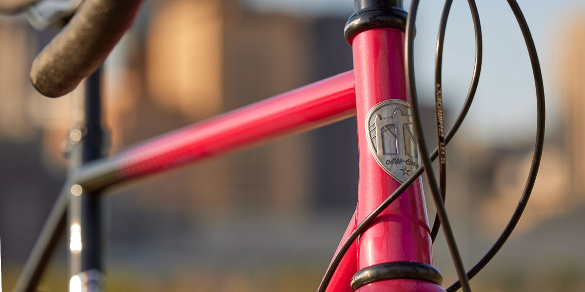 Front three-quarter view of pink and black All-City Cycles Zig Zag Ultegra complete bike, close-up of headbadge