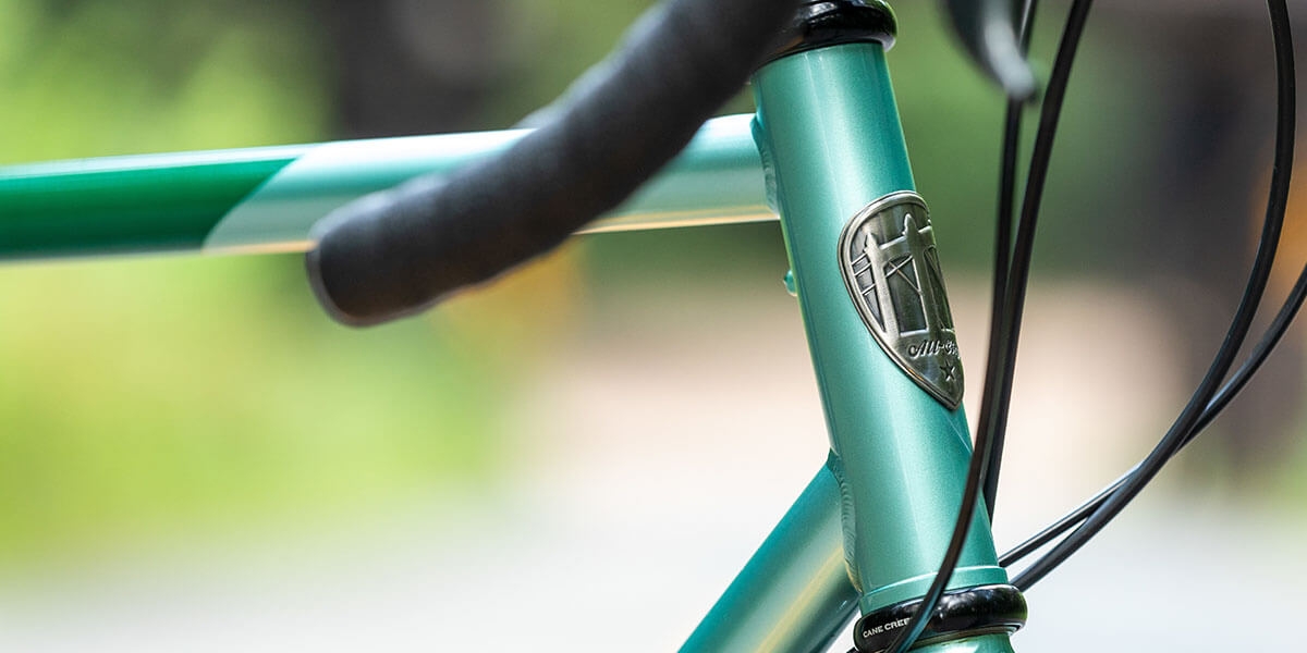 All-City green Spacehorse bike, close up head tube and head badge view with an outdoor background