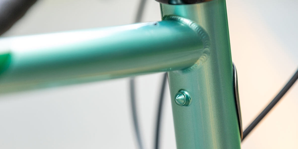 All-City green Spacehorse bike, close up of top tube and heat tube junction with pump peg with an outdoor background