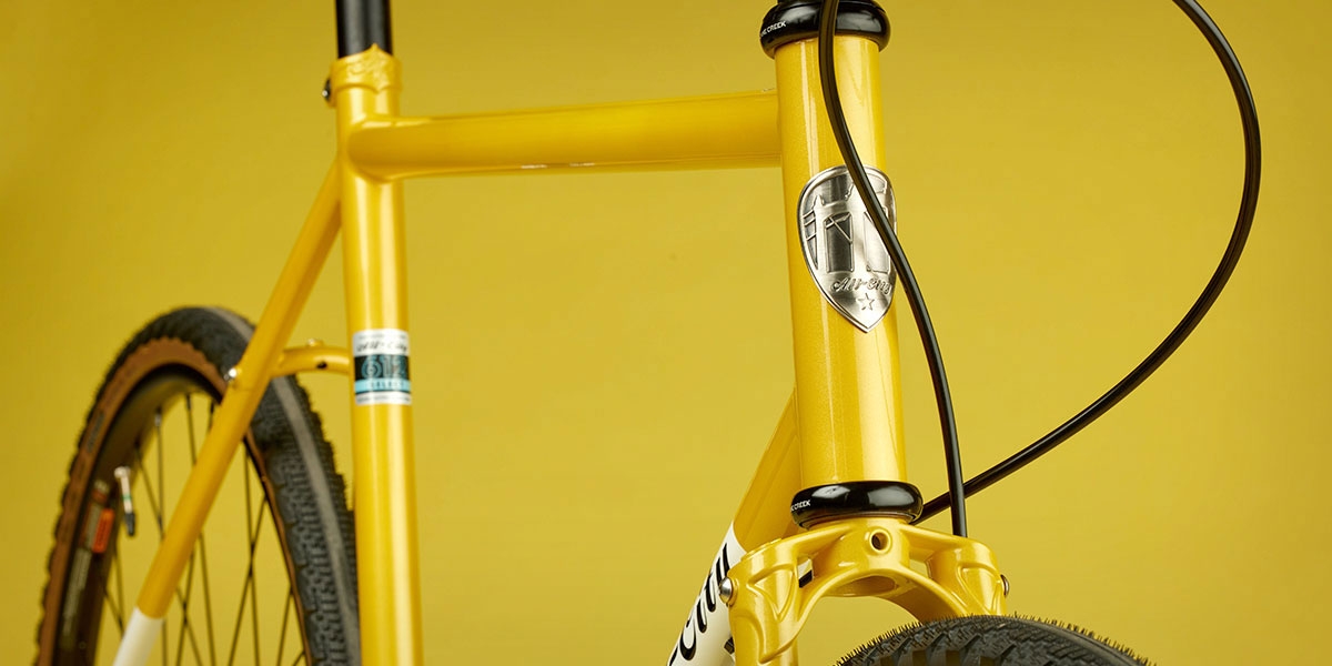 All-City Cycles Super Professional Single Speed bike side view in Yellow Dab color focus on headtube badge and fork crown
