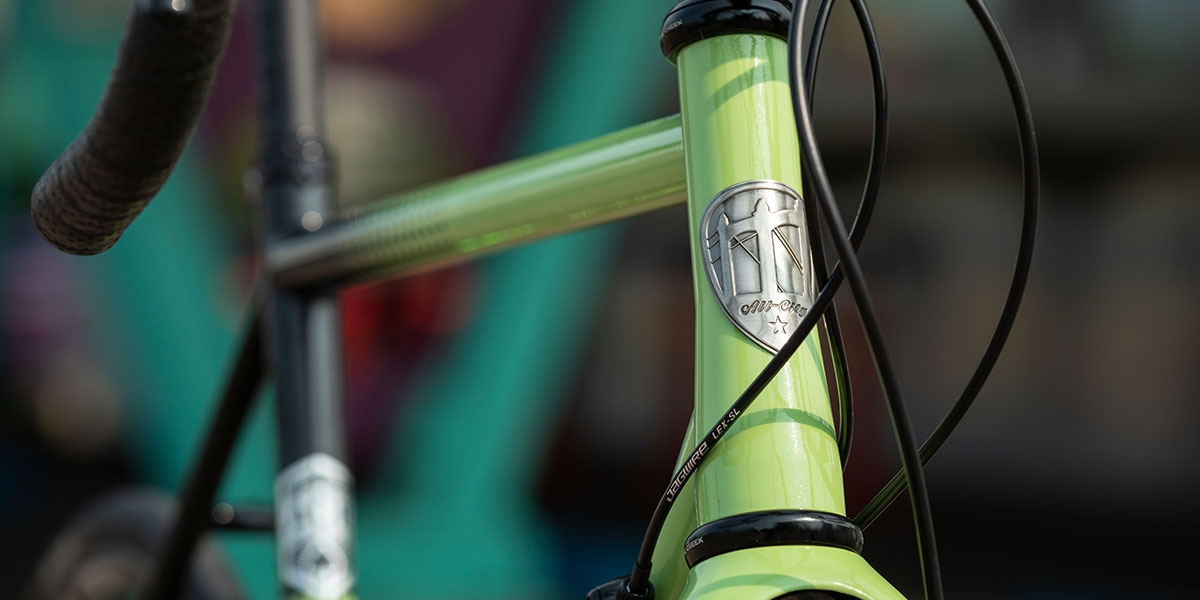 Front three-quarter view of green and black All-City Cycles Zig Zag 105 complete bike, close-up of headbadge