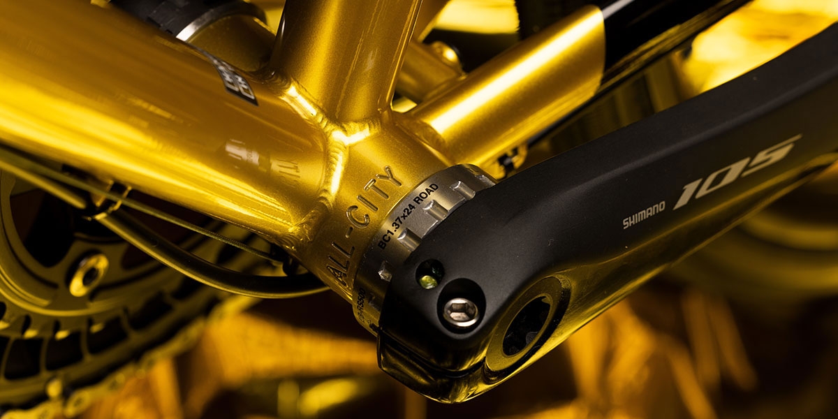 Close-up of All-City stamped in bottom bracket shell of gold All-City Zig Zag 105 bike, cranks and BB installed