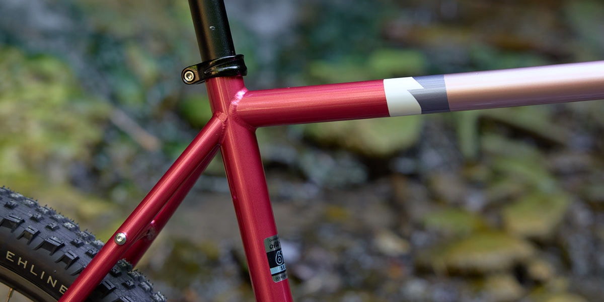 All-City Gorilla Monsoon in Hotberry Rhubarb color, dropper seatpost, top tube, seat tube, seatstay detail against outdoor background