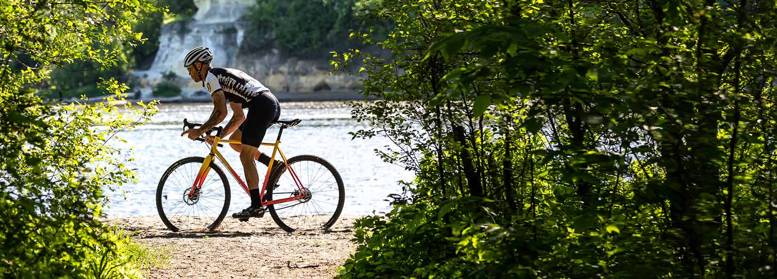 Person in cycling apparel and helmet riding Nature Cross Single Speed on sandy river shoreline