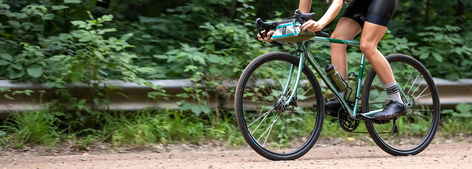 Person riding All-City SpaceHorse green bike outside on gravel, focus on bike