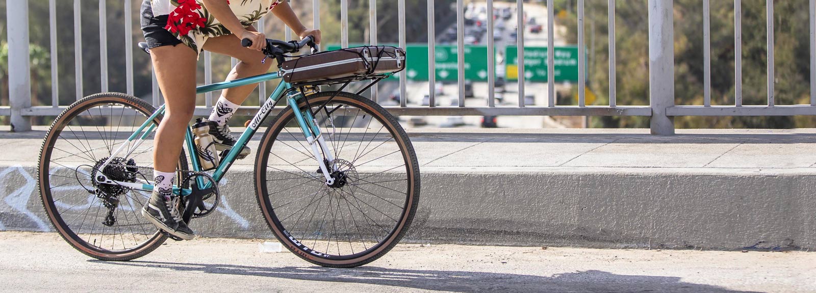 Cyclist riding All-City Super Professional across highway bridge with briefcase on front rack, focus on bike