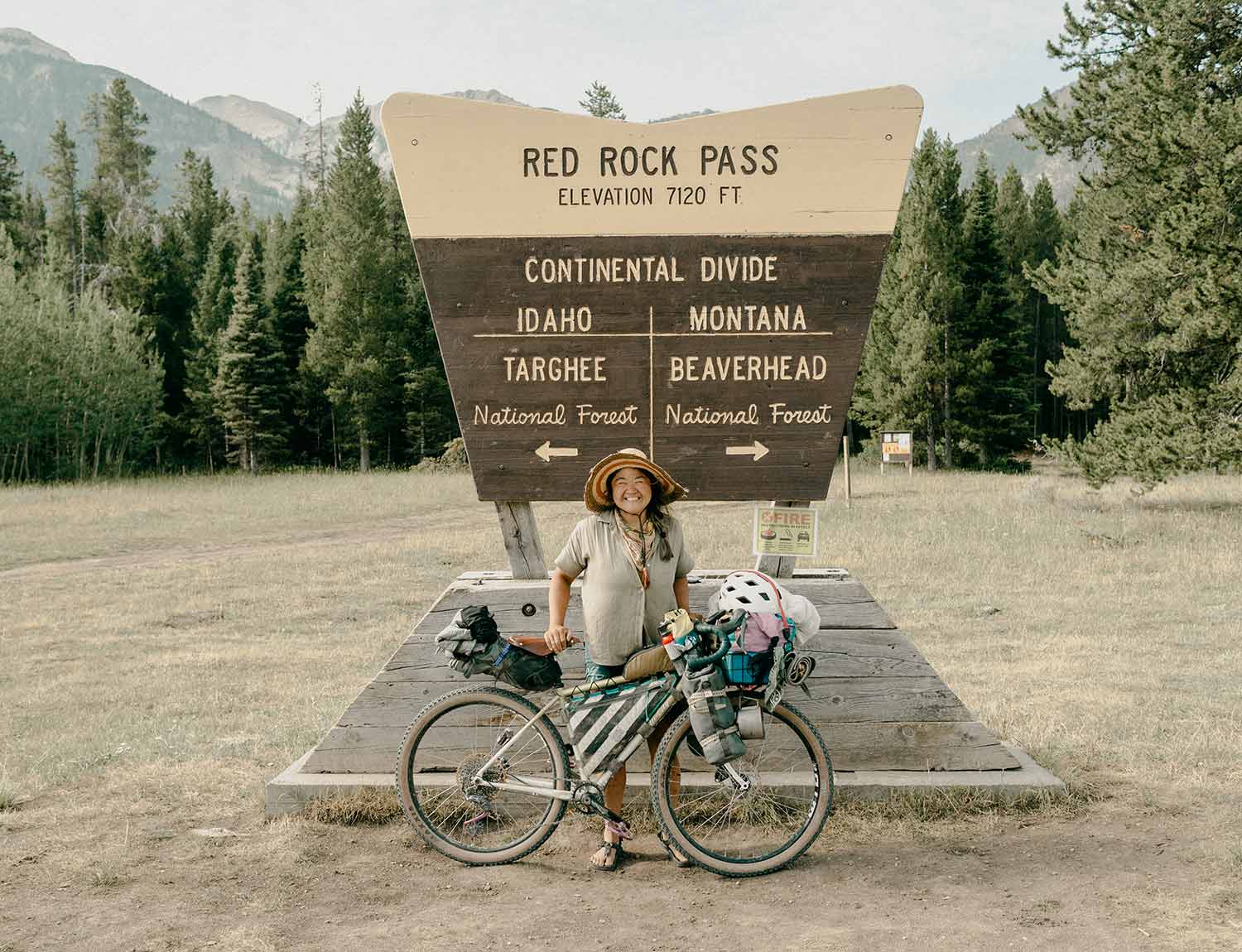 Kae-Lin Wang with fully-loaded bike in front of Red Rock Pass sign on the continental divide