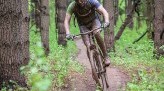 Pat Goretraill wears a black helmet and jersey to ride through a green woodsy trail