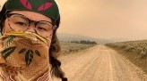 Kae-Lin selfie on gravel road wearing handkerchief over nose and mouth to protect against wildfire smoke, haze in distance