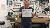 Lauren Rothering holds bicycle and assembly certificate, smiling with bike shop background