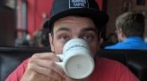 Pat Goretraill wears red shirt and black hat while looking into the camera and drinking from a white mug