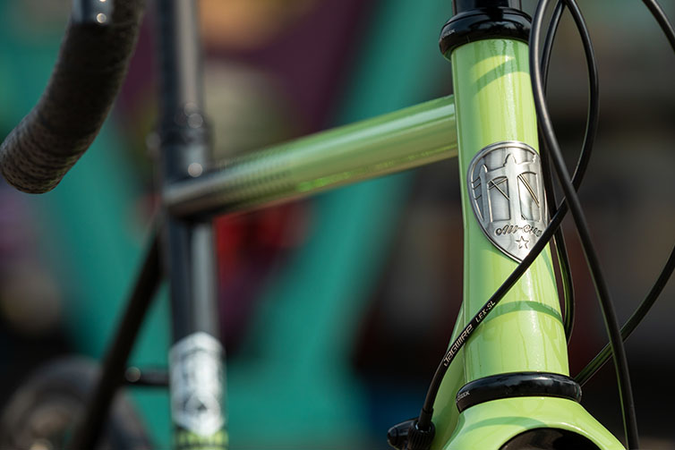 Front three-quarter view of green and black All-City Cycles Zig Zag 105 complete bike, close-up of headbadge