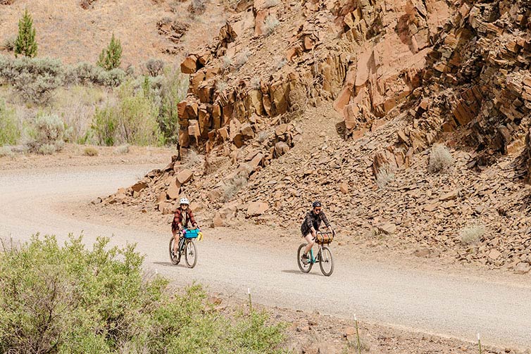 Two cyclists riding Gorilla Monsoon bikes on remote desert gravel road in the mountains on sunny day