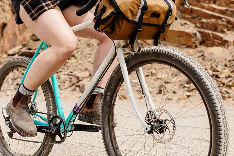 Person riding Gorilla Monsoon bike in Aqua Seafoam color on rocky desert road with front bag attached to handlebar