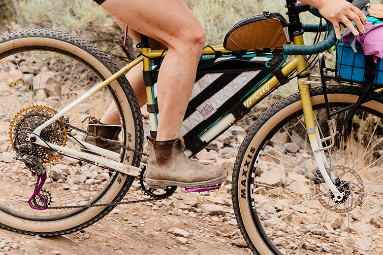 Close up of Wang riding Gorilla Monsoon with frame bags and front rack on rocky desert road, focus on bike