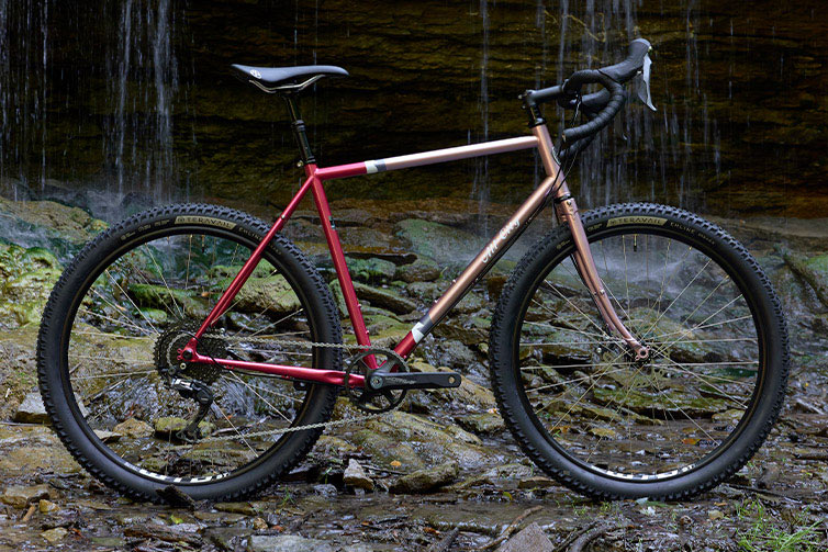 All-City Gorilla Monsoon GRX bike in Hotberry Rhubarb colorway in front of rocky waterfalll