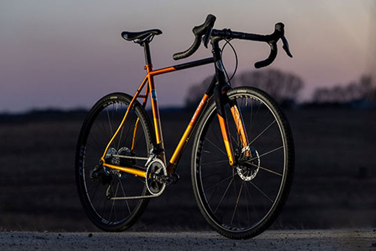 All-City Cosmic Stallion Rival AXS Wide complete bike, front three-quarter view on gravel road at sun set