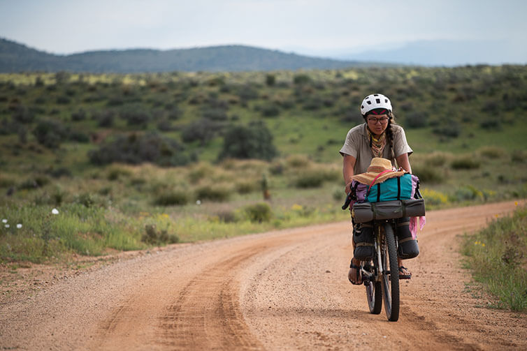Kae-Lin Wang riding loaded Gorilla Monsoon bike on gravel road, prairie and hills in background