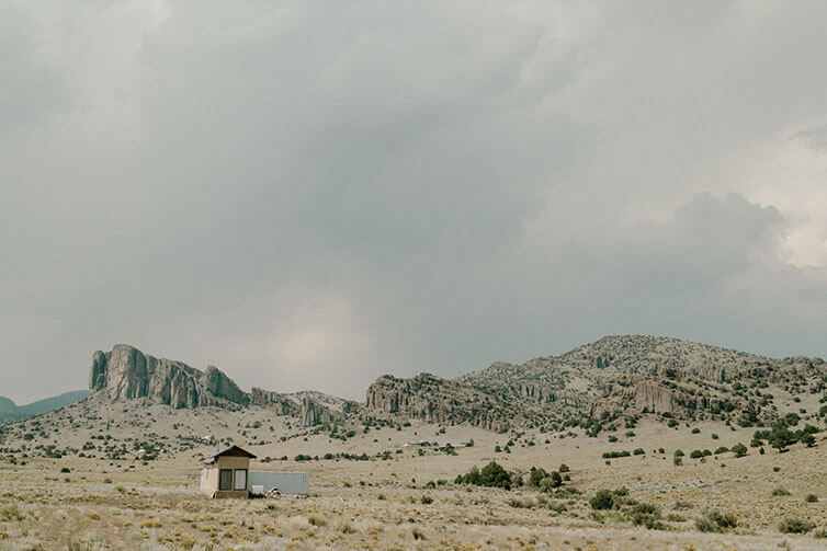 High elevation desert with hills and rocky outcrops and small home, storm clouds brewing