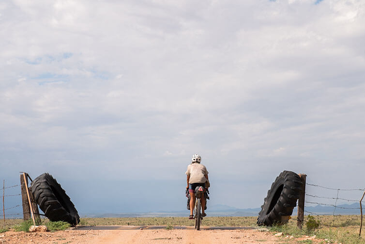 Kae-Lin riding high plains gravel road across cattle guard, barbed wire fence and huge tractor tires on either side