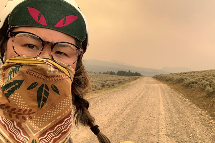 Kae-Lin selfie on gravel road wearing handkerchief over nose and mouth to protect against wildfire smoke, haze in distance