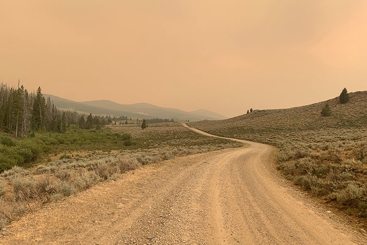 Gravel road through valley, smoke haze everywhere, mountains in distance