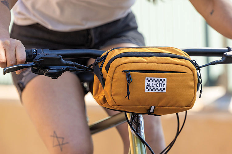 Person riding bike with All-City Turntable Sling Bag mounted on handlebars of bike