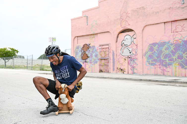 Leo Rodgers rides small fake horse in front of graffiti building