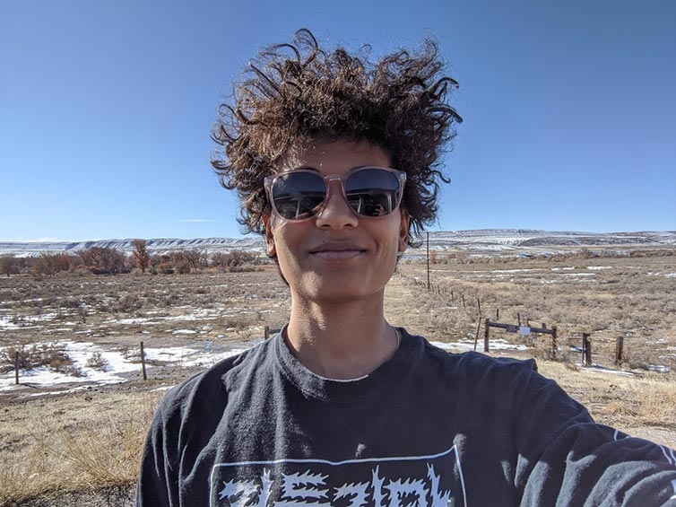 Selfie of Endria on sunny day wearing sunglasses with snowy prairie and hills in background