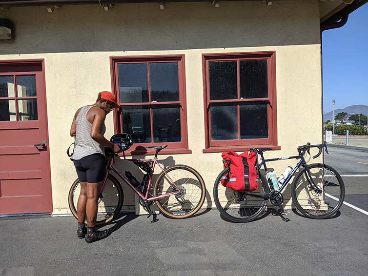 Grace in cycling apparel pulling gear from loaded bike parked against building on sunny day