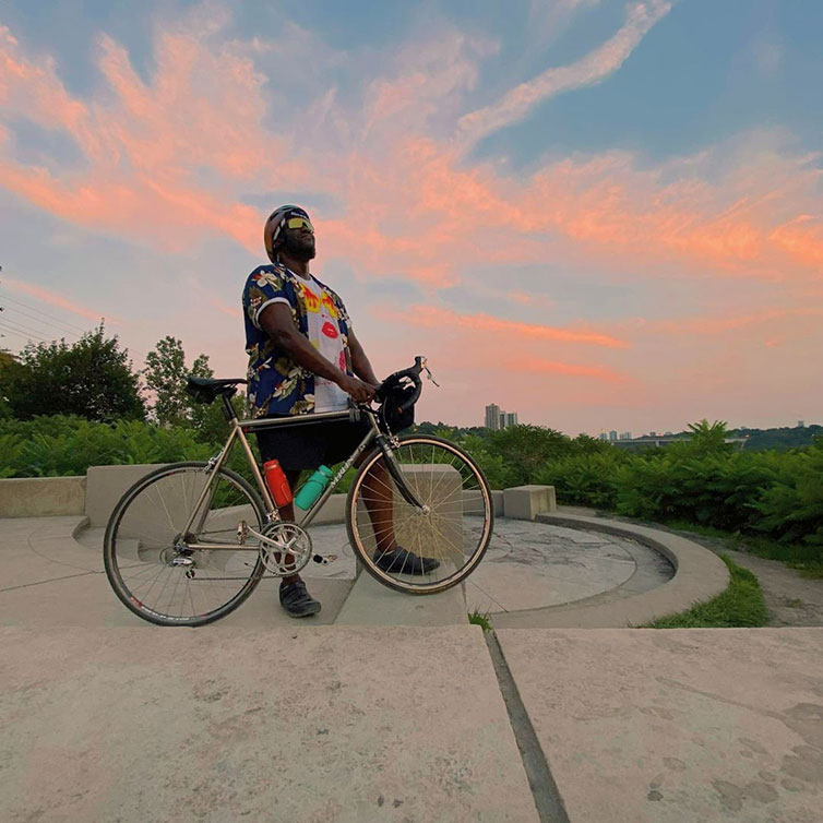 Person standing with bike during sunset looking up at sky, at overlook concrete structure