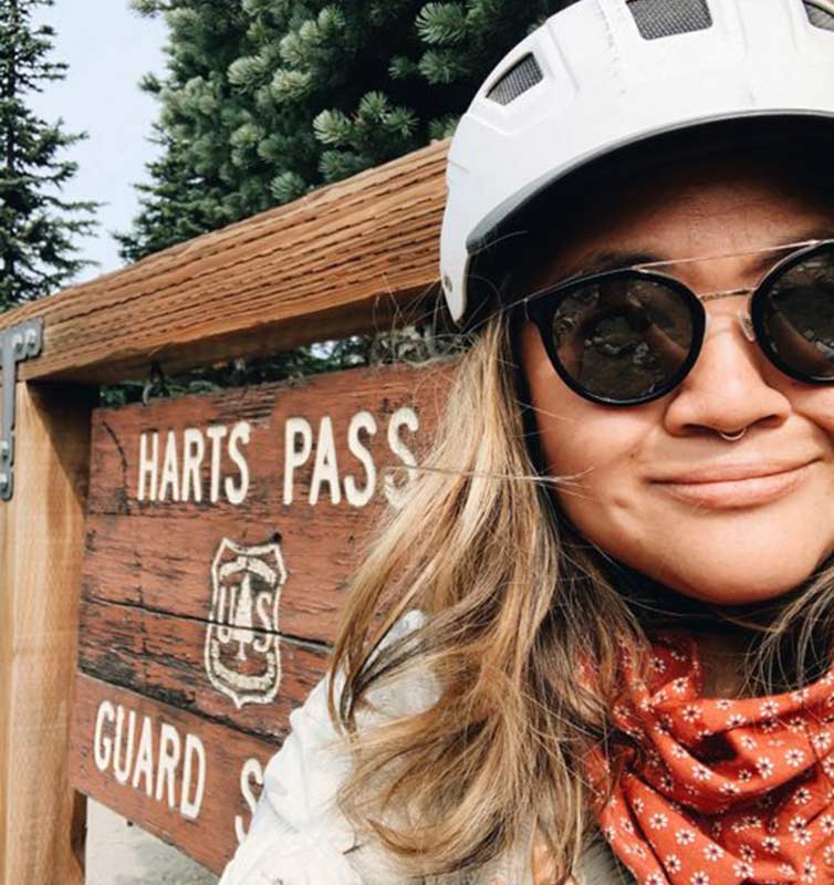 Karen Wang selfie with bike helmet and glasses on in front of Harts Pass sign