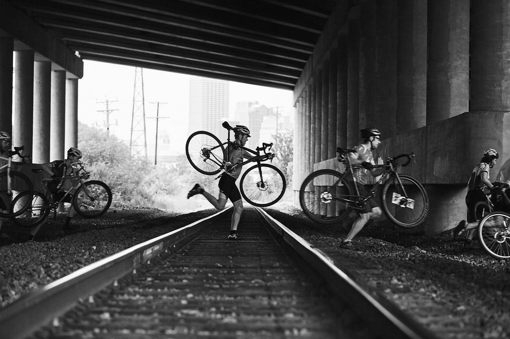 Riders Carrying Bikes Over a Railroad