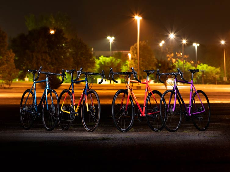 Six All-City Cycles silhouetted agains orange and yellow nighttime lights