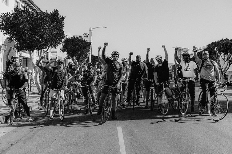 Ron Holden standing over a bike in a crowd with one fist raised at Ride For Black Lives event