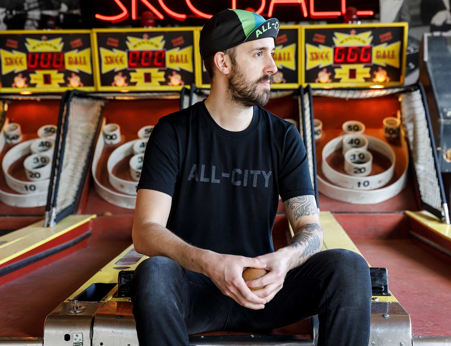 Person wears black All-City Cycles Travel Wool Shirt in front of skee ball lanes