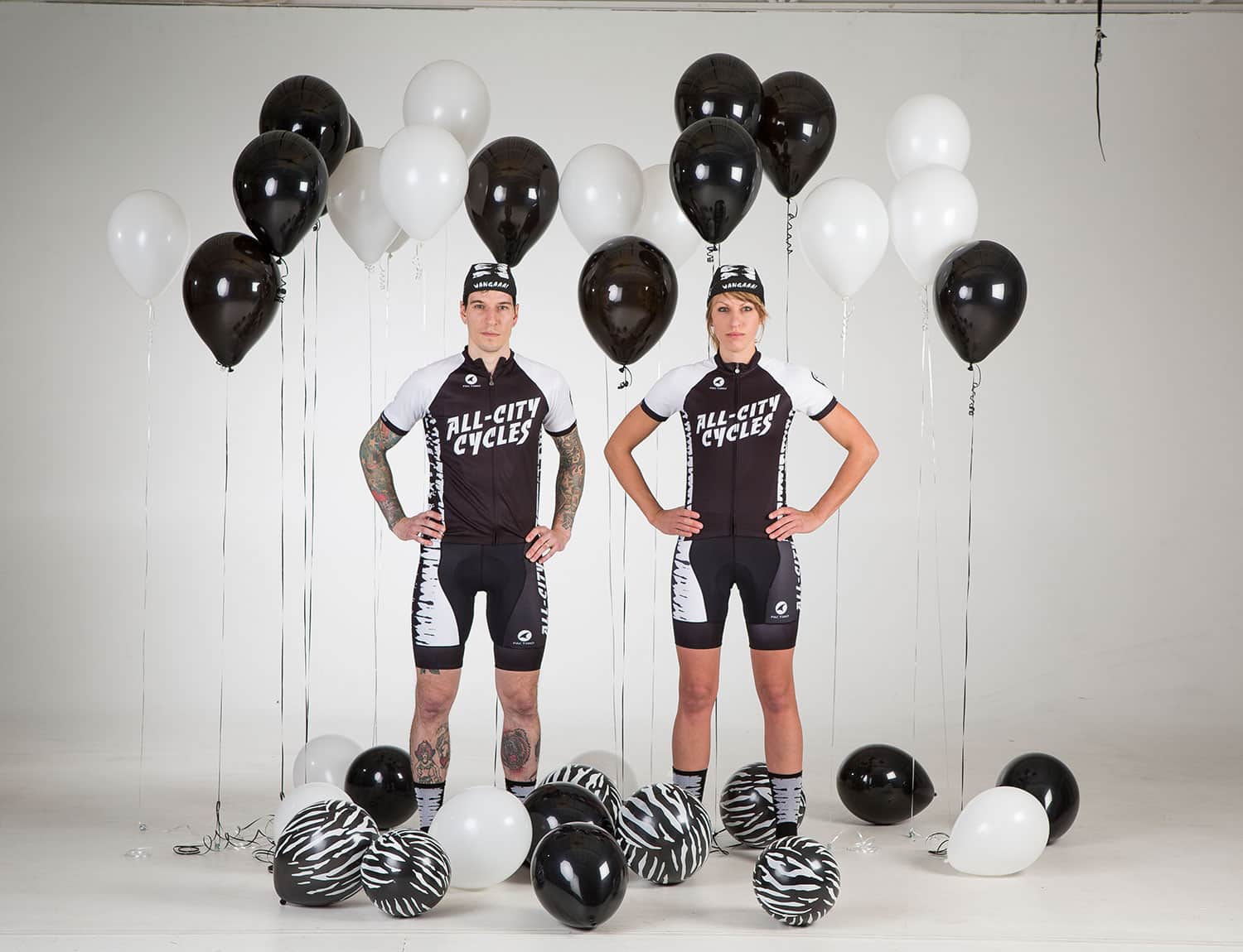 Two people with hands on hips wearing black and white All-City Wangaaa Jerseys with balloons around them