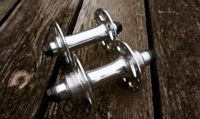 Two polished Silver All-City New Sheriff SL Front track racing hubs on wheel with brick background
