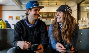 Two people sitting and smiling wearing black and white All-City Cycles Tu Tone Neck Gaiter