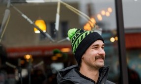 Person wearing green and black All-city Angry catfish sledding cap in front of window