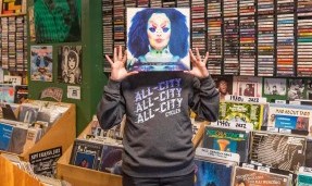Person wearing Blue All-City flow motion t-shirt holding record up to face