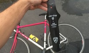 Hand holding black All-City foldable fender over pink bike