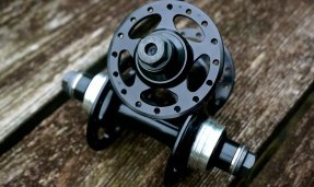 One polished silver and one black All-City New Sheriff SL Front hubs on wood background side view