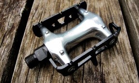 all city black and polished silver standard track pedal against wood background