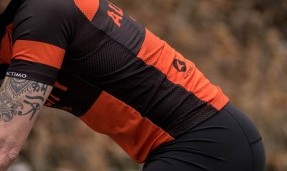 Side of a person wearing black and orange All-City classic jersey 2.0 walking through trail