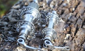 Two polished silver All-City Go-Devil Rear Rim Brake Hubs front view on outdoor rock 