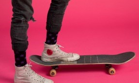 Person wearing black let's Go Crazy Socks while skateboarding on pink background side view