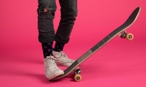 Person wearing black let's Go Crazy Socks while skateboarding on pink background stepping on back