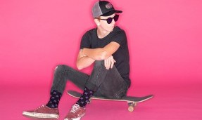 Person wearing black let's Go Crazy Socks sitting on skateboard on pink background