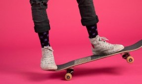 Person wearing black let's Go Crazy Socks while skateboarding on pink background